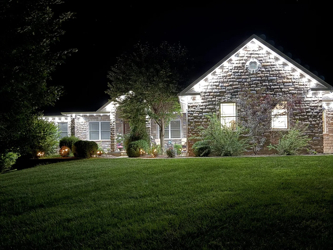 Permanent eave lighting in warm white outlining the roofline of a stone home, installed by Freedom Electric